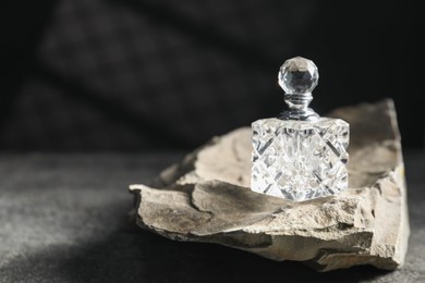 Photo of Bottle of fragrant perfume and rock on grey table, space for text