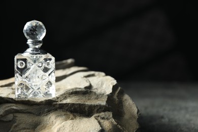 Photo of Bottle of fragrant perfume and rock on grey table, space for text