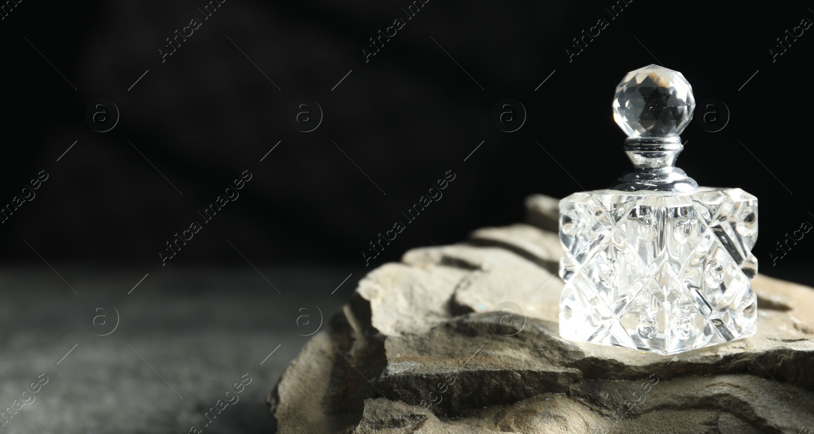 Photo of Bottle of fragrant perfume and rock on grey table, space for text