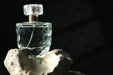 Photo of Bottle of fragrant perfume on rock against dark background, space for text