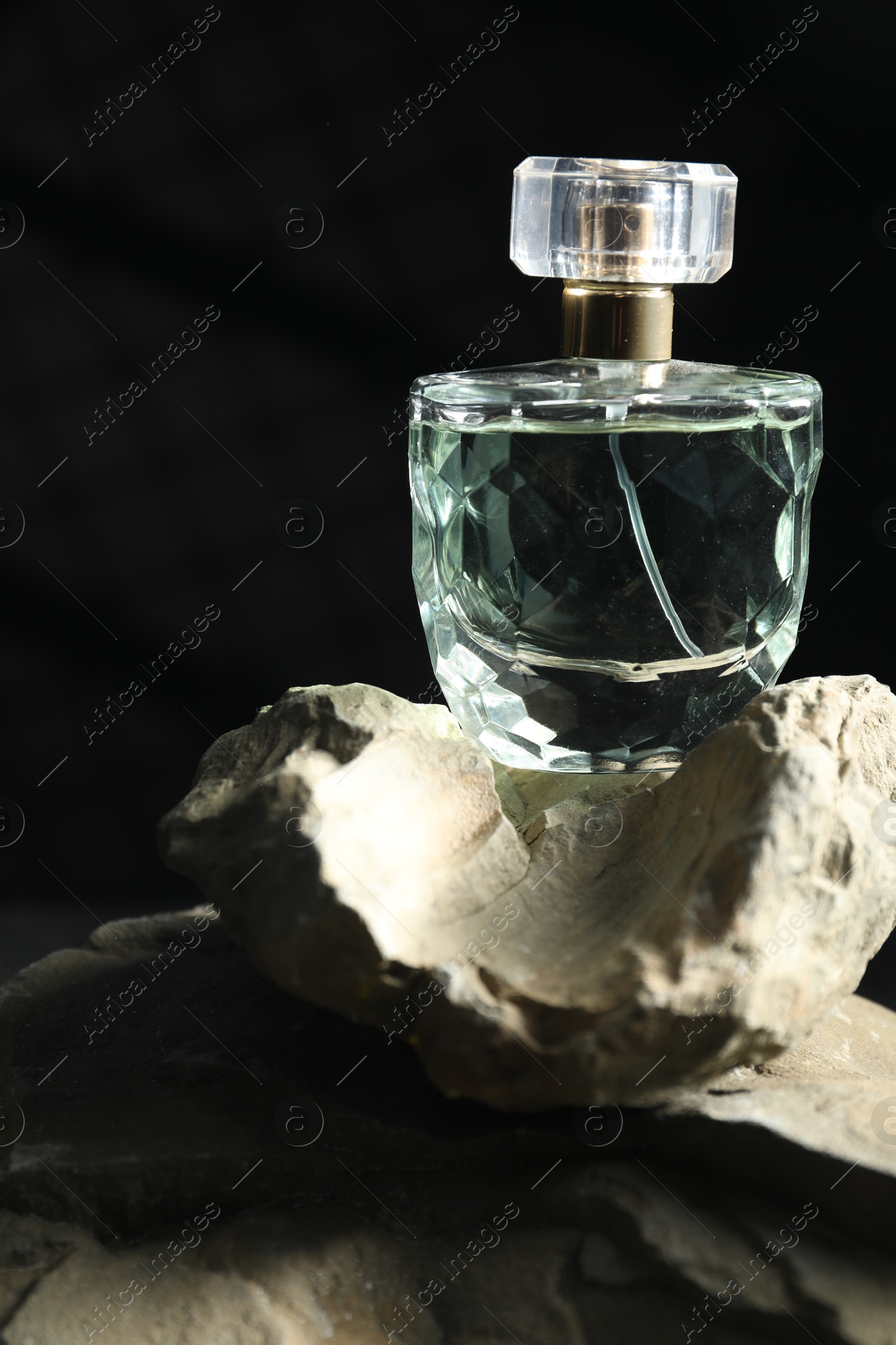 Photo of Bottle of fragrant perfume on rock against dark background