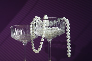 Photo of Elegant wine glasses and pearl jewelry on purple background, low angle view