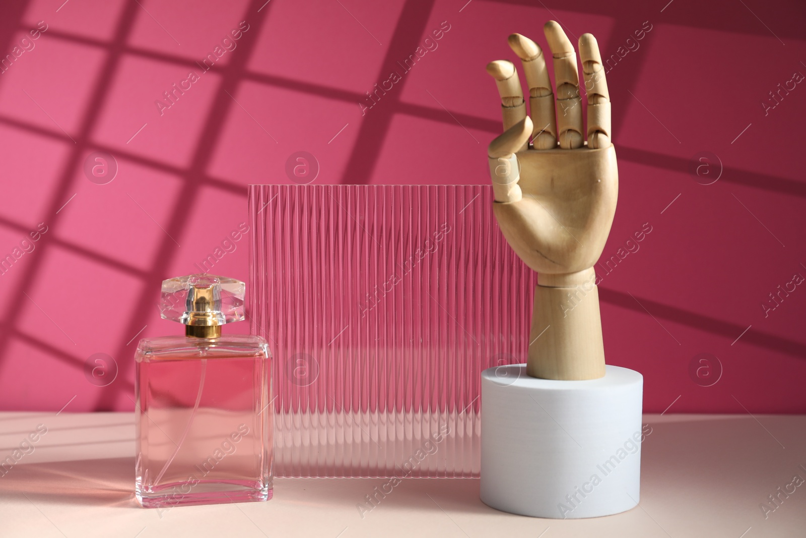 Photo of Bottle of fragrant perfume and wooden mannequin hand on pink background