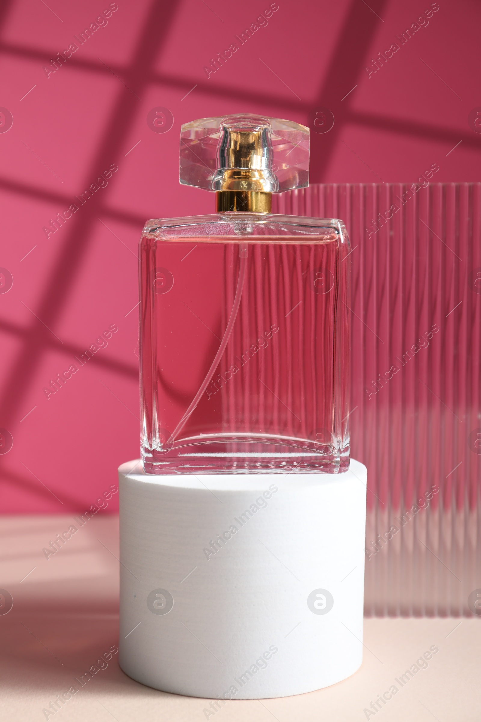 Photo of Stylish presentation of perfume bottle on white table against pink background