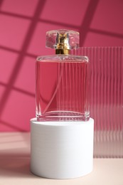 Photo of Stylish presentation of perfume bottle on white table against pink background