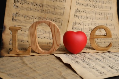 Photo of Word Love made of wooden letters and heart with musical notes on black background