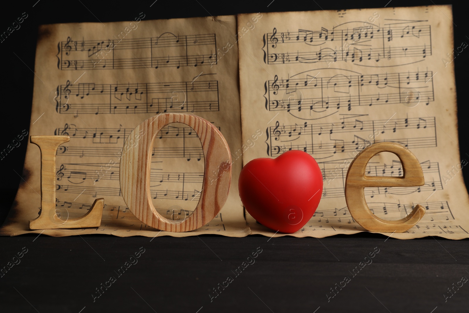 Photo of Word Love made of wooden letters and heart with musical notes on black background