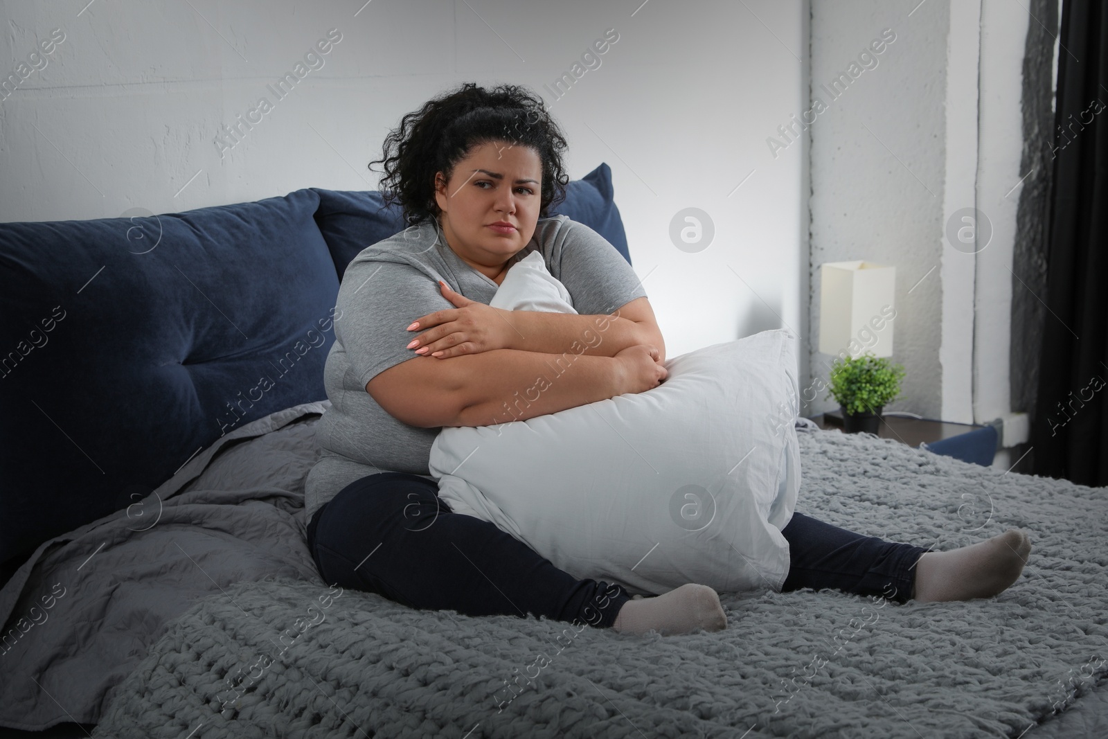 Image of Depressed overweight woman hugging pillow on bed