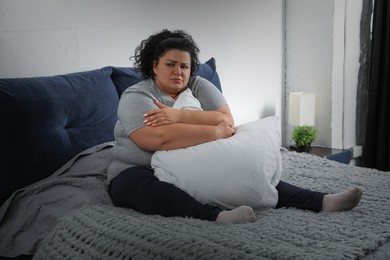 Depressed overweight woman hugging pillow on bed