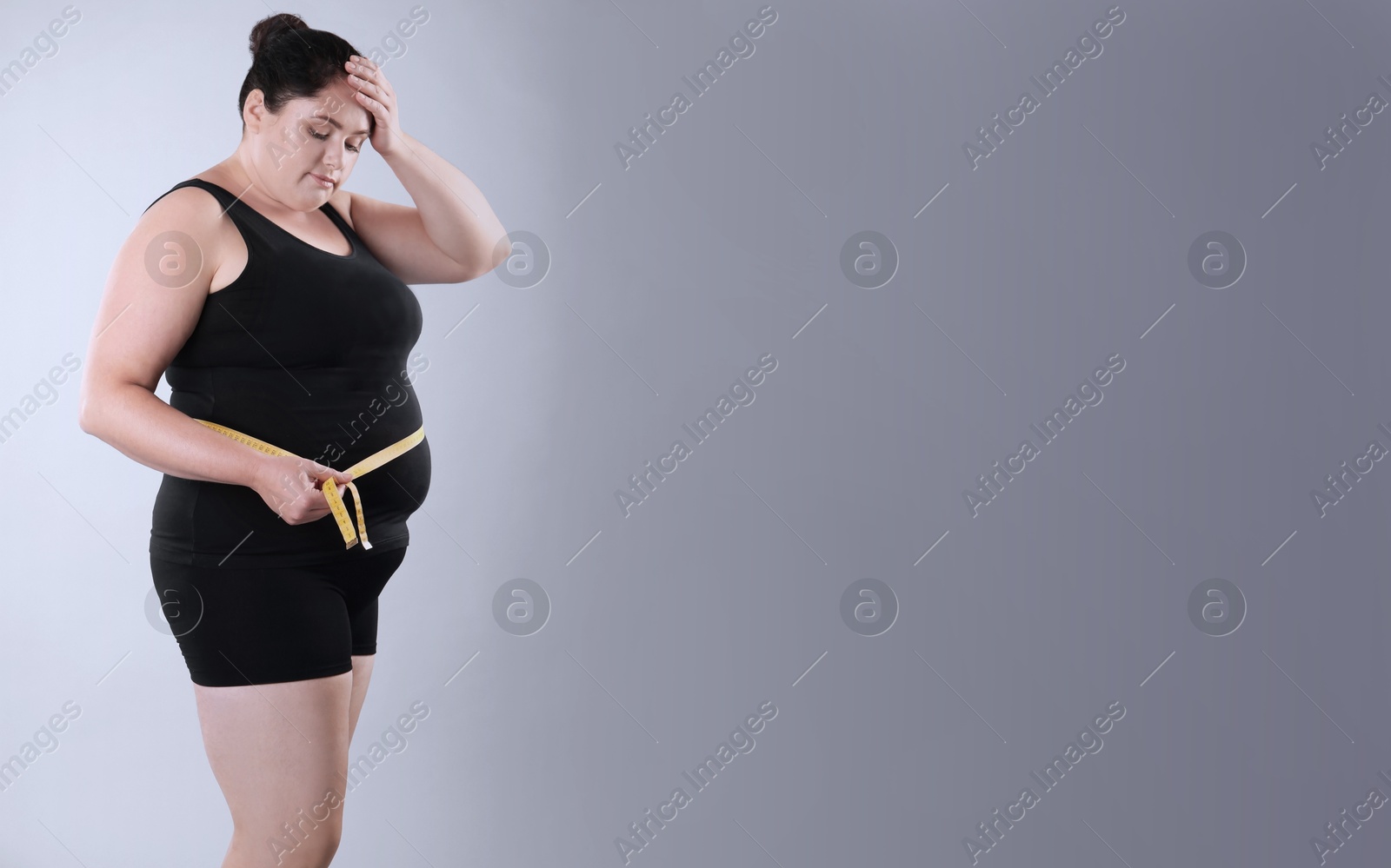 Image of Unhappy overweight woman with measuring tape on grey background, space for text