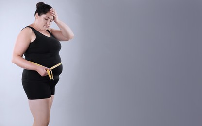 Unhappy overweight woman with measuring tape on grey background, space for text