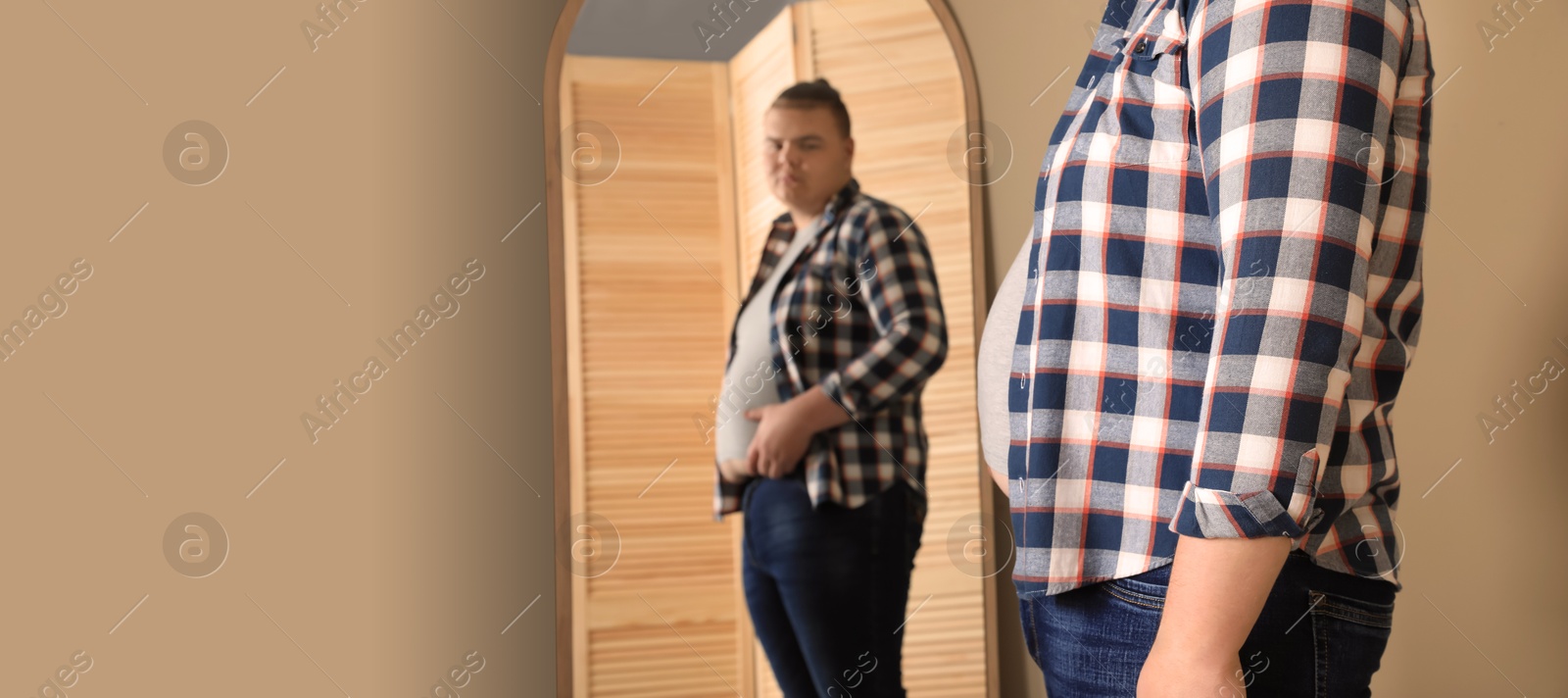 Image of Overweight man in tight t-shirt near mirror at home. Banner design with space for text