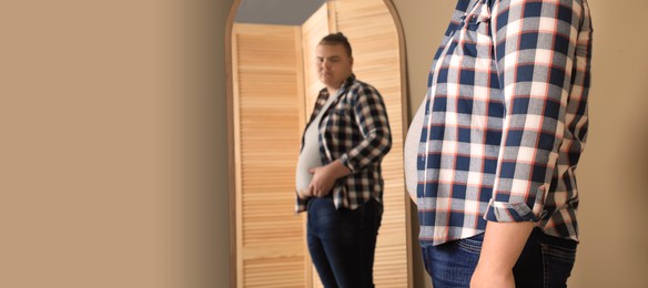 Image of Overweight man in tight t-shirt near mirror at home. Banner design with space for text