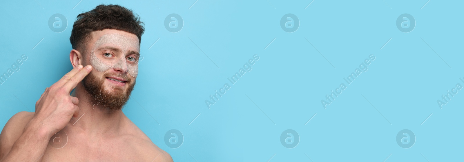 Image of Young man applying mask on face against light blue background. Banner design with space for text. Skin care