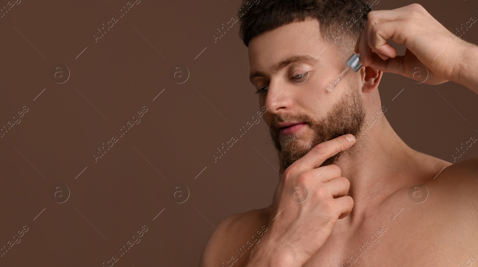 Image of Young man applying serum on face against brown background. Banner design with space for text. Skin care