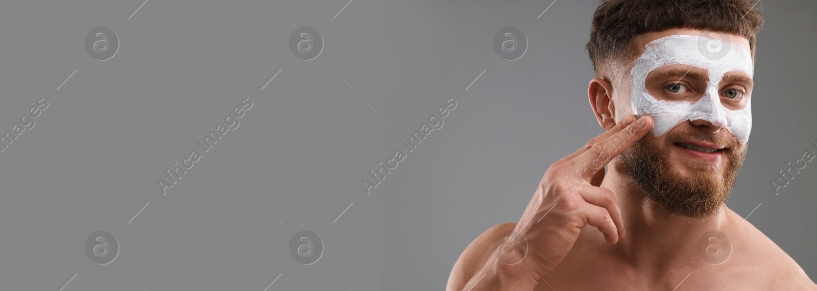 Image of Young man applying mask on face against grey background. Banner design with space for text. Skin care