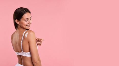 Beautiful woman applying cream onto skin against pink background. Banner design with space for text. Body care