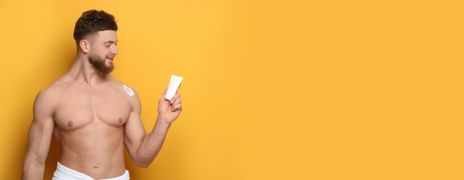 Young man with cream against orange background. Banner design with space for text. Skin care