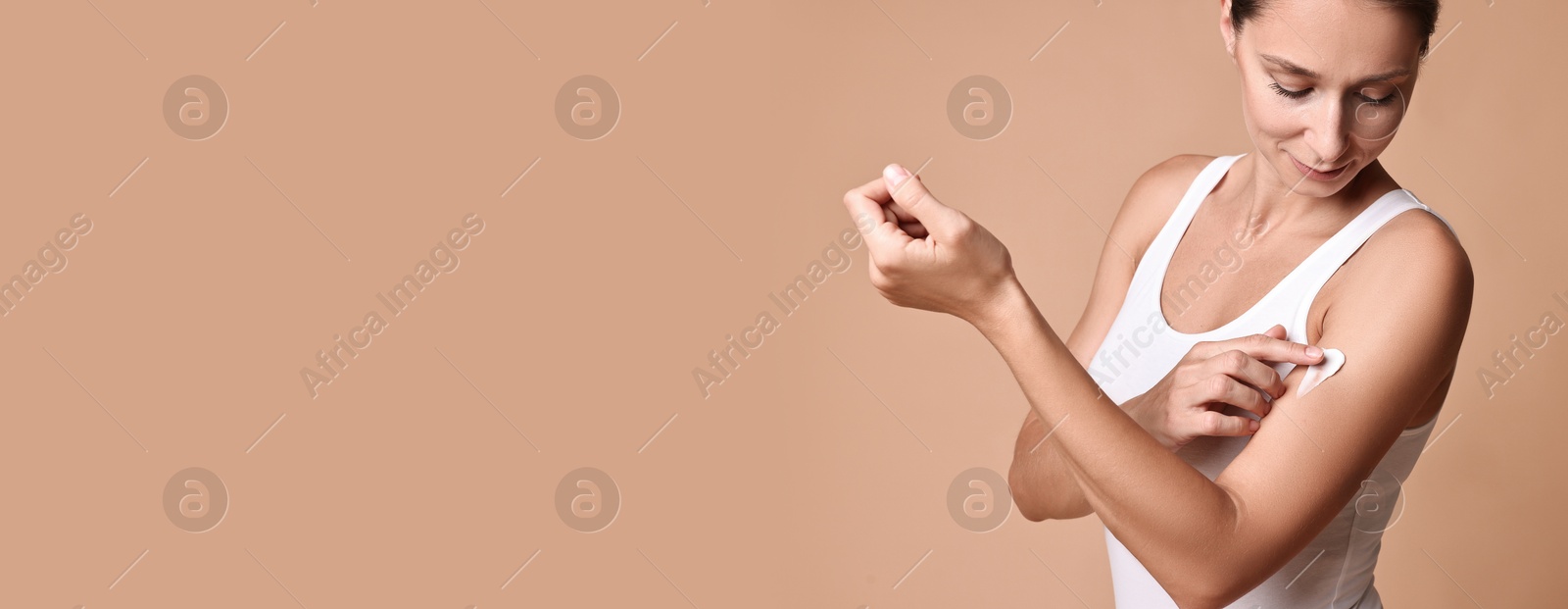 Image of Beautiful woman applying cream onto skin against dark beige background. Banner design with space for text. Body care