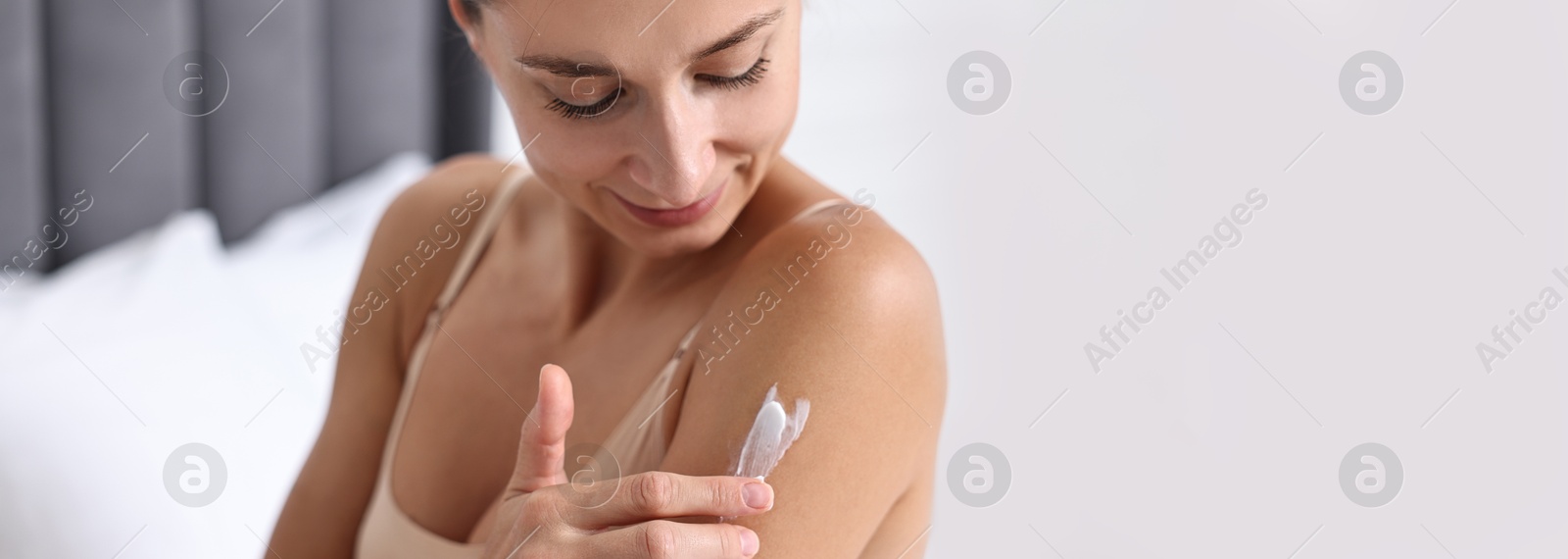 Image of Beautiful woman applying cream onto skin indoors, closeup. Banner design with space for text. Body care