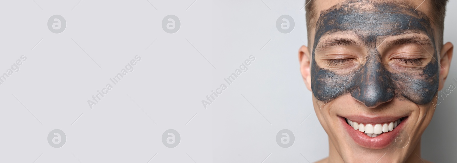 Image of Young man with mask on his face against light grey background, closeup. Banner design with space for text. Skin care