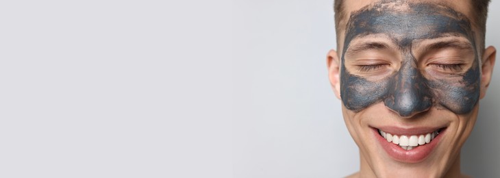 Image of Young man with mask on his face against light grey background, closeup. Banner design with space for text. Skin care