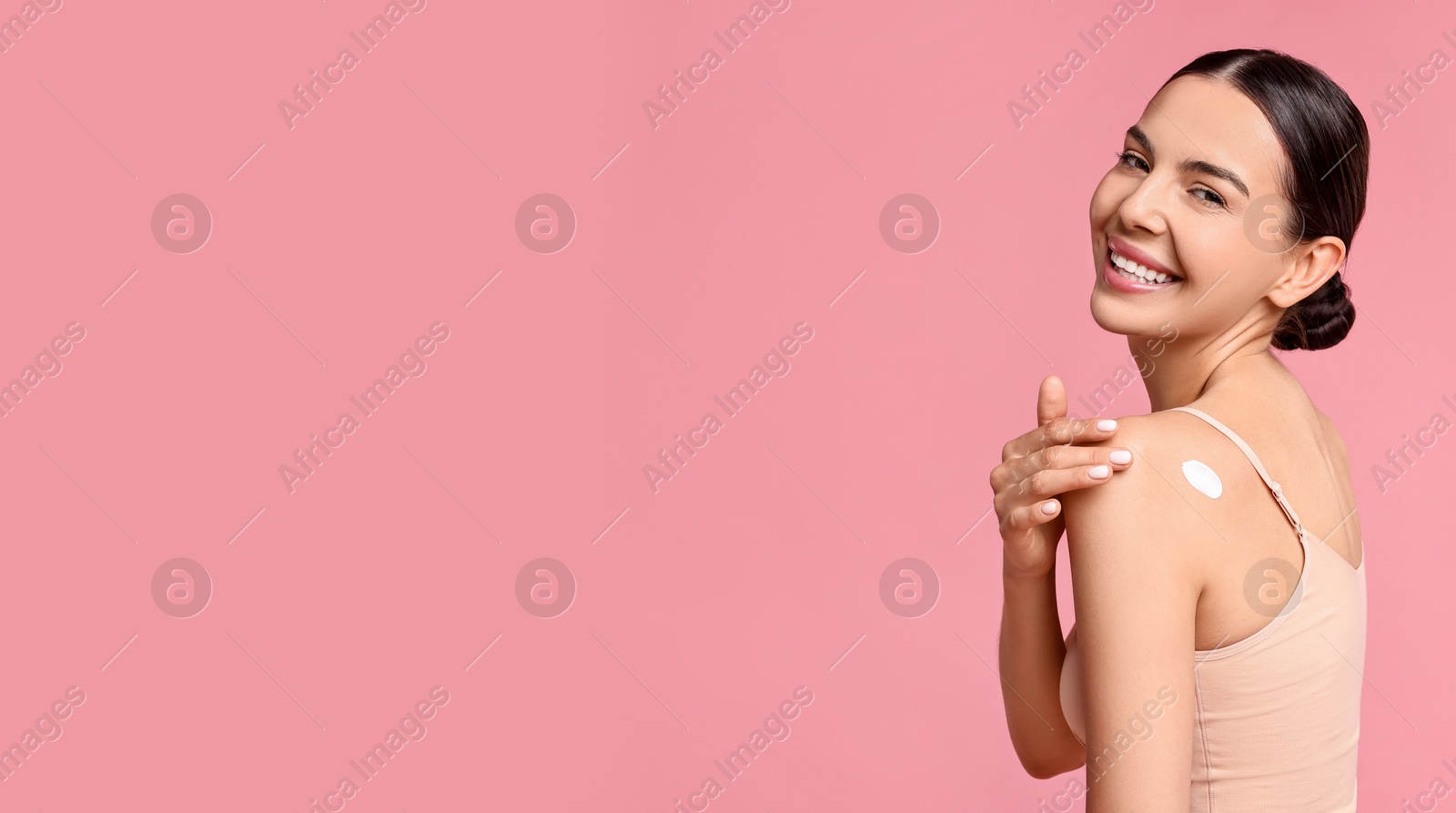 Image of Young woman applying cream onto skin against pink background. Banner design with space for text. Body care