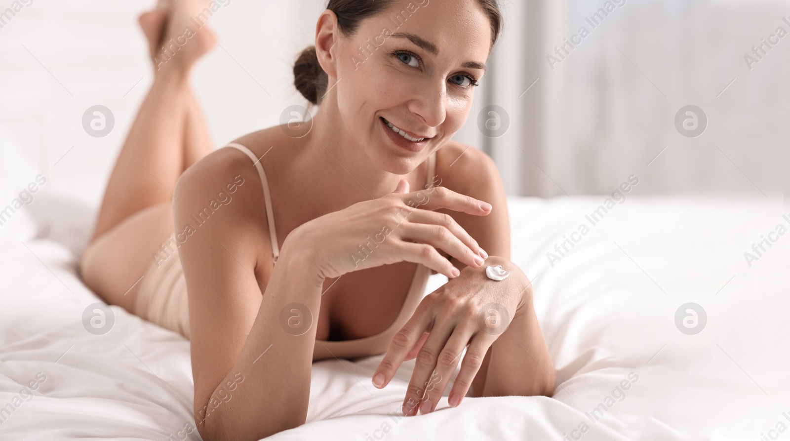 Image of Beautiful woman applying cream onto skin on bed. Banner design with space for text. Body care