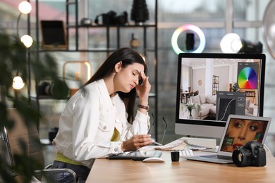 Photo of Tired retoucher at table with modern computer and laptop in office