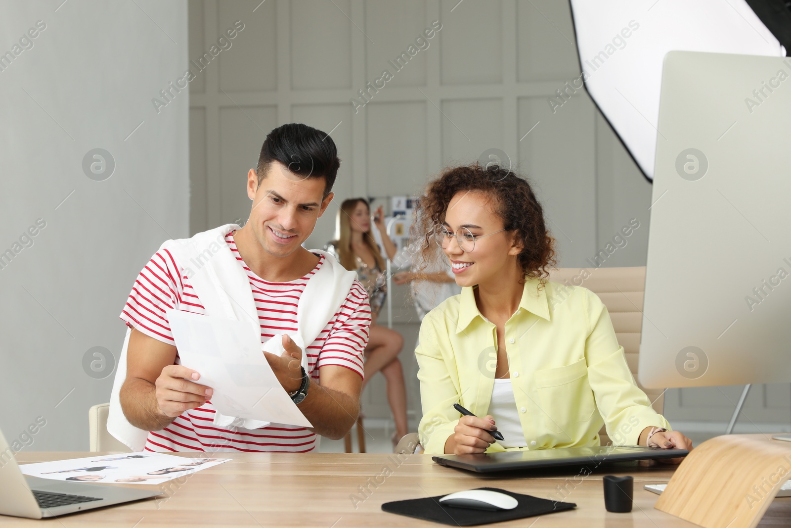 Photo of Professional retoucher with colleague working at desk in photo studio