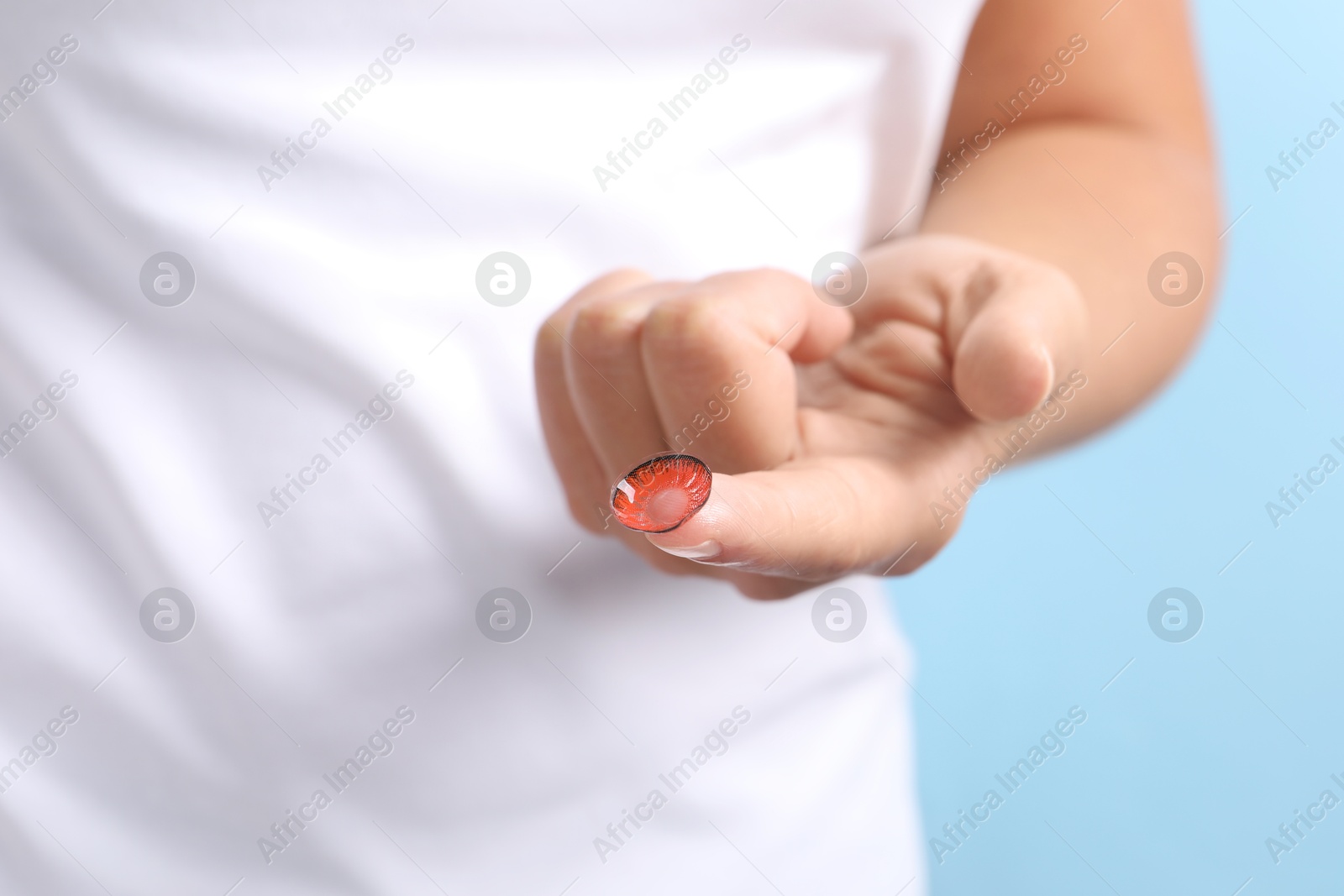 Photo of Woman holding color contact lens on light blue background, closeup