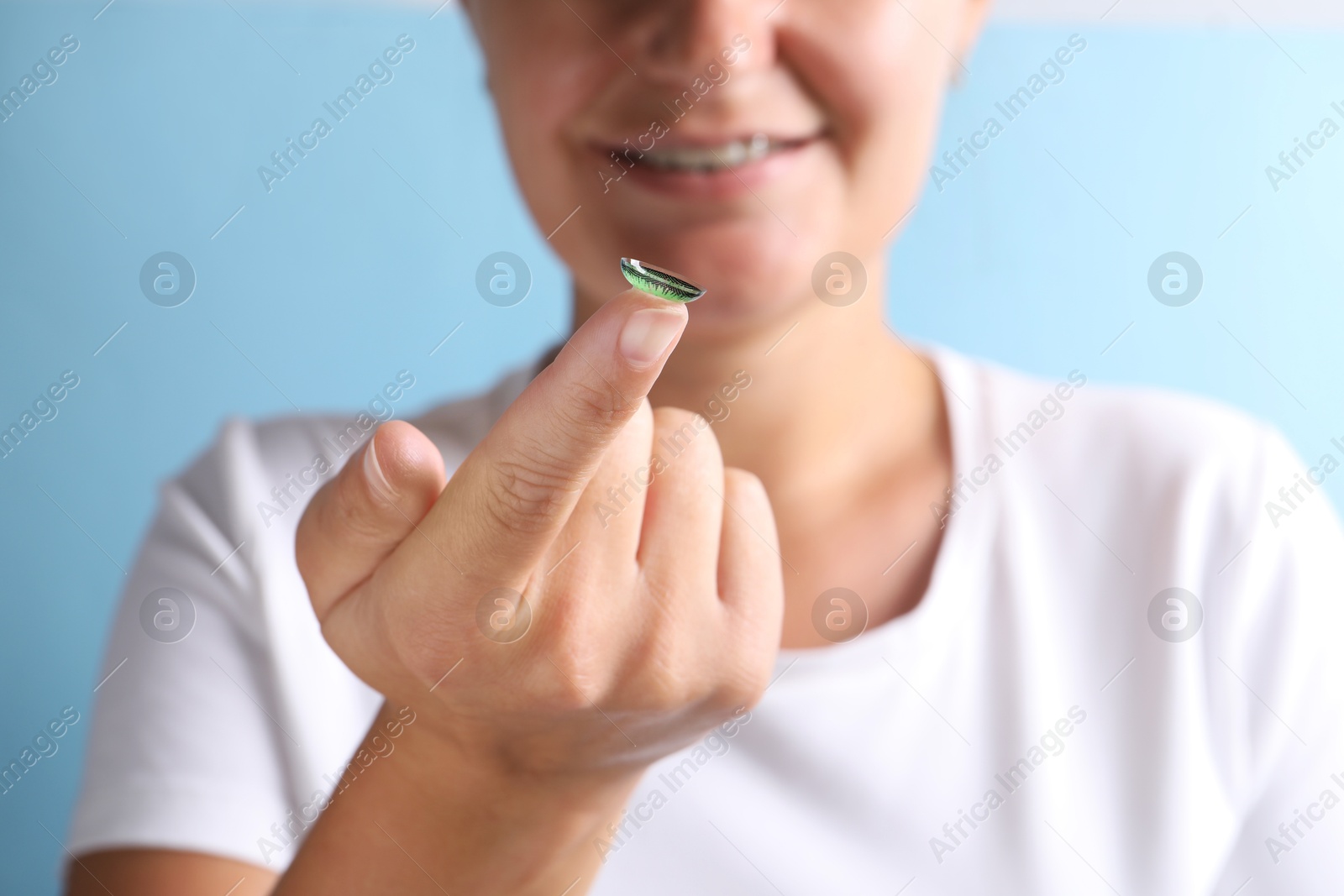 Photo of Woman holding color contact lens on light blue background, closeup