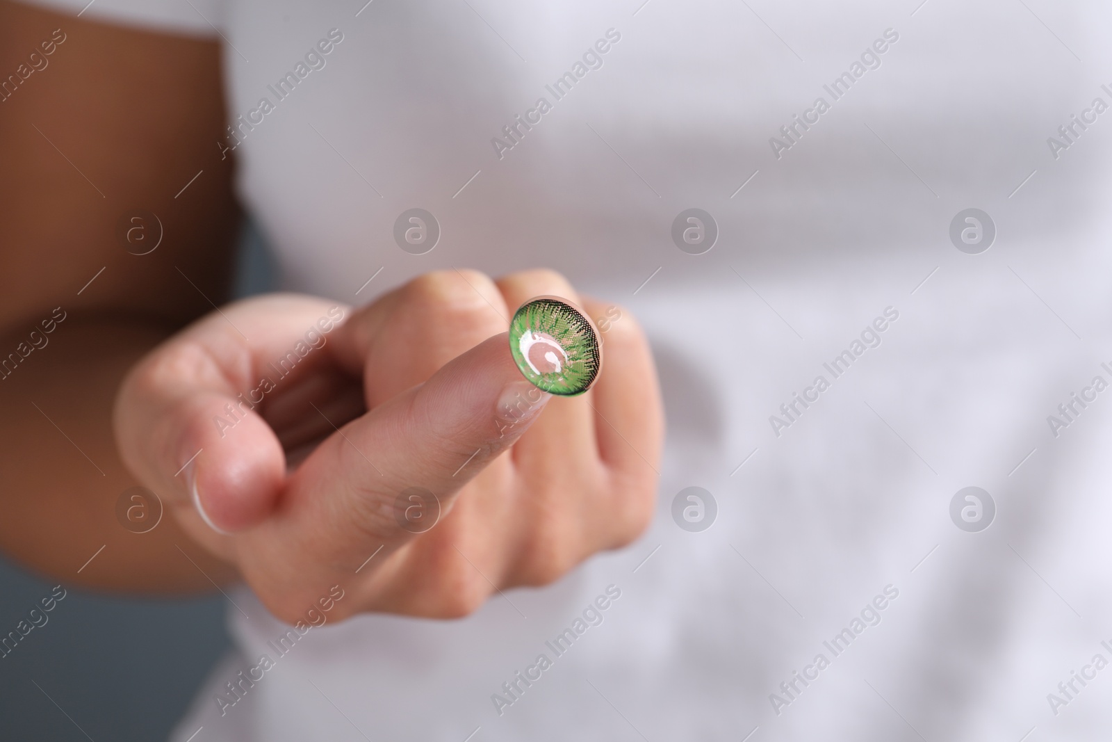 Photo of Woman holding color contact lens on light background, closeup