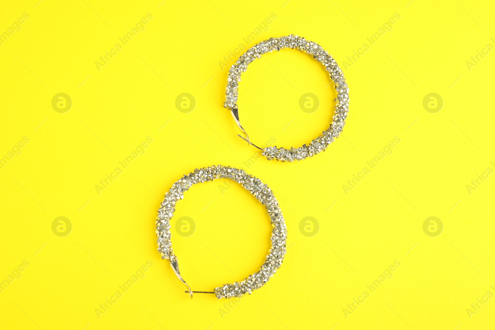 Photo of Beautiful bijouterie. Stylish earrings on yellow background, top view