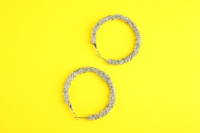 Photo of Beautiful bijouterie. Stylish earrings on yellow background, top view