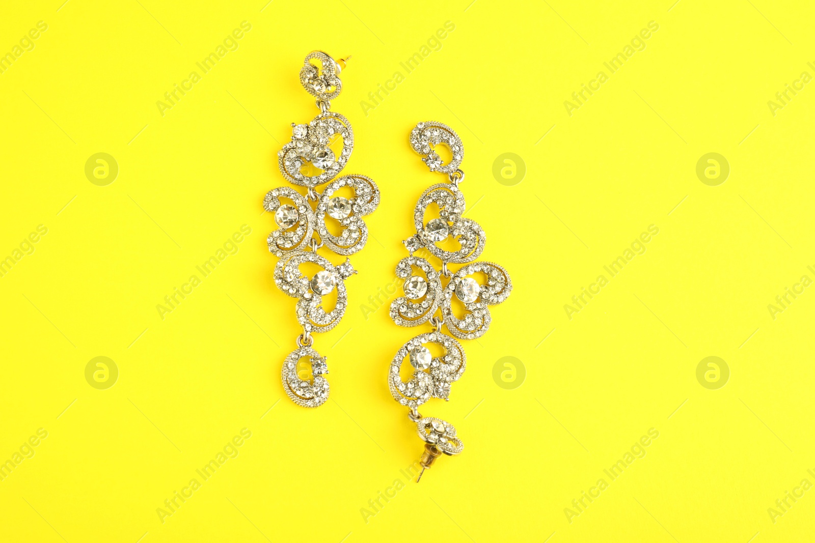 Photo of Beautiful bijouterie. Stylish earrings on yellow background, top view