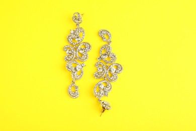 Photo of Beautiful bijouterie. Stylish earrings on yellow background, top view