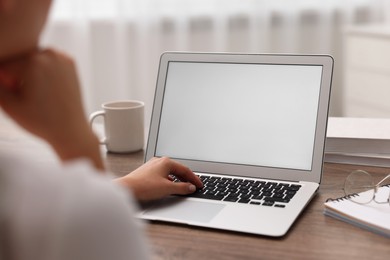 Photo of Woman working with laptop at wooden table in office, closeup. Mockup for design