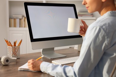 Photo of Woman working with computer monitor at wooden table in office, closeup. Mockup for design