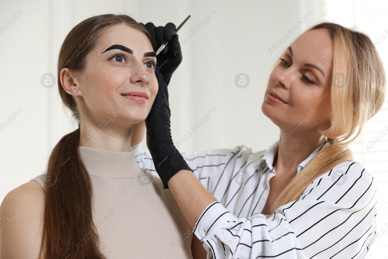 Photo of Beautician dyeing client’s eyebrows with henna in salon