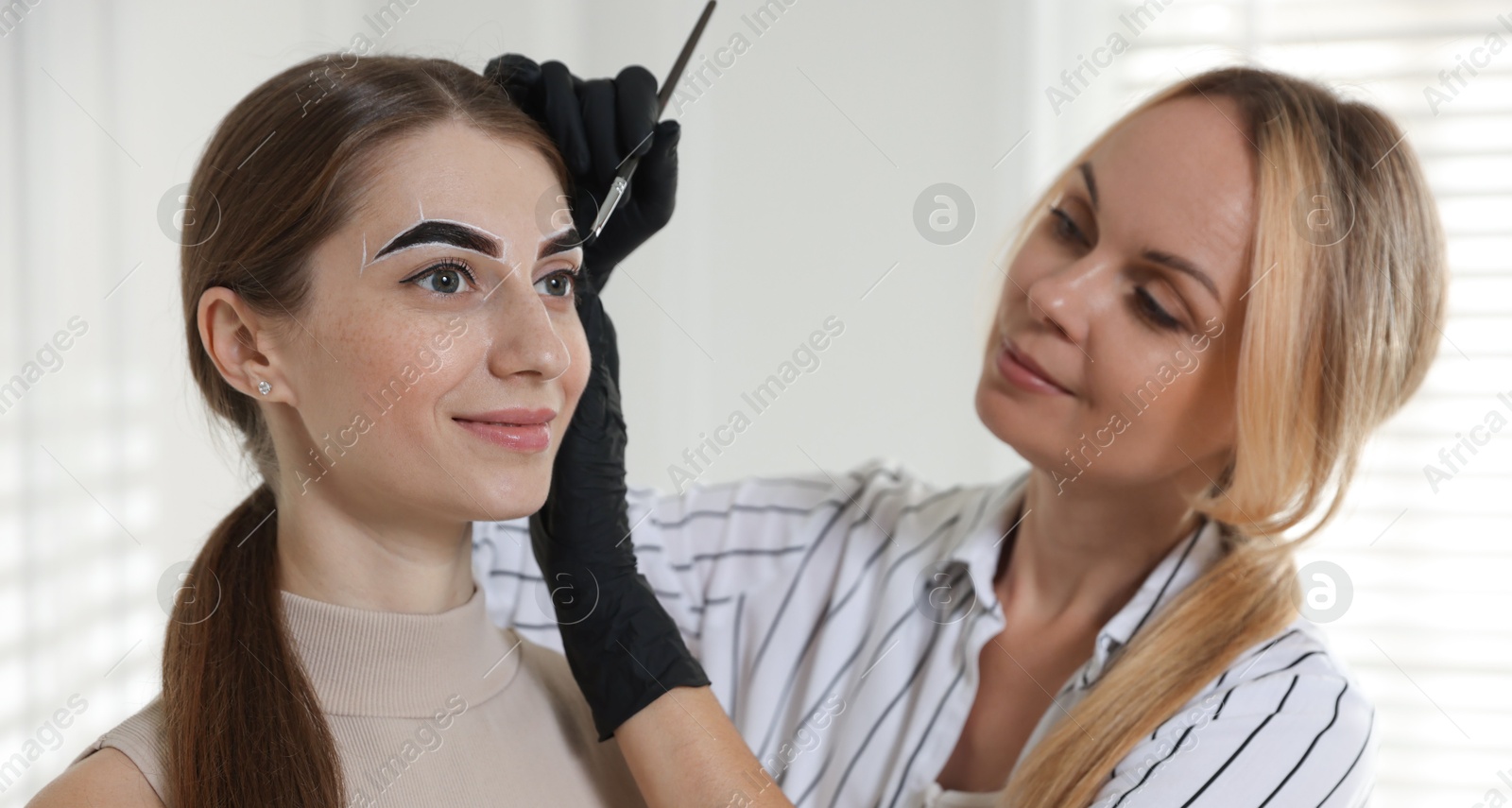 Photo of Beautician dyeing client’s eyebrows with henna in salon, selective focus