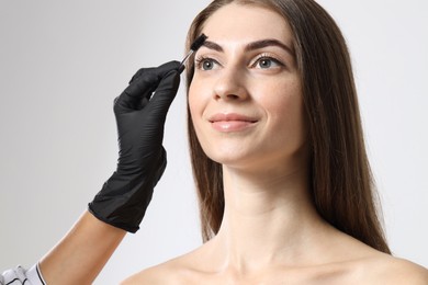 Photo of Beautician brushing client's eyebrows after henna dyeing procedure on light background, closeup