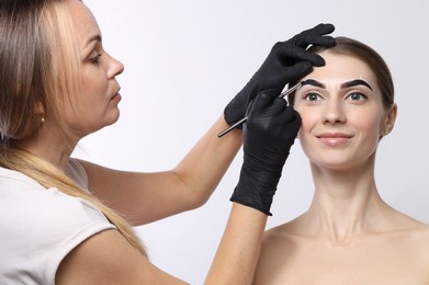 Photo of Beautician dyeing client’s eyebrows with henna on light background