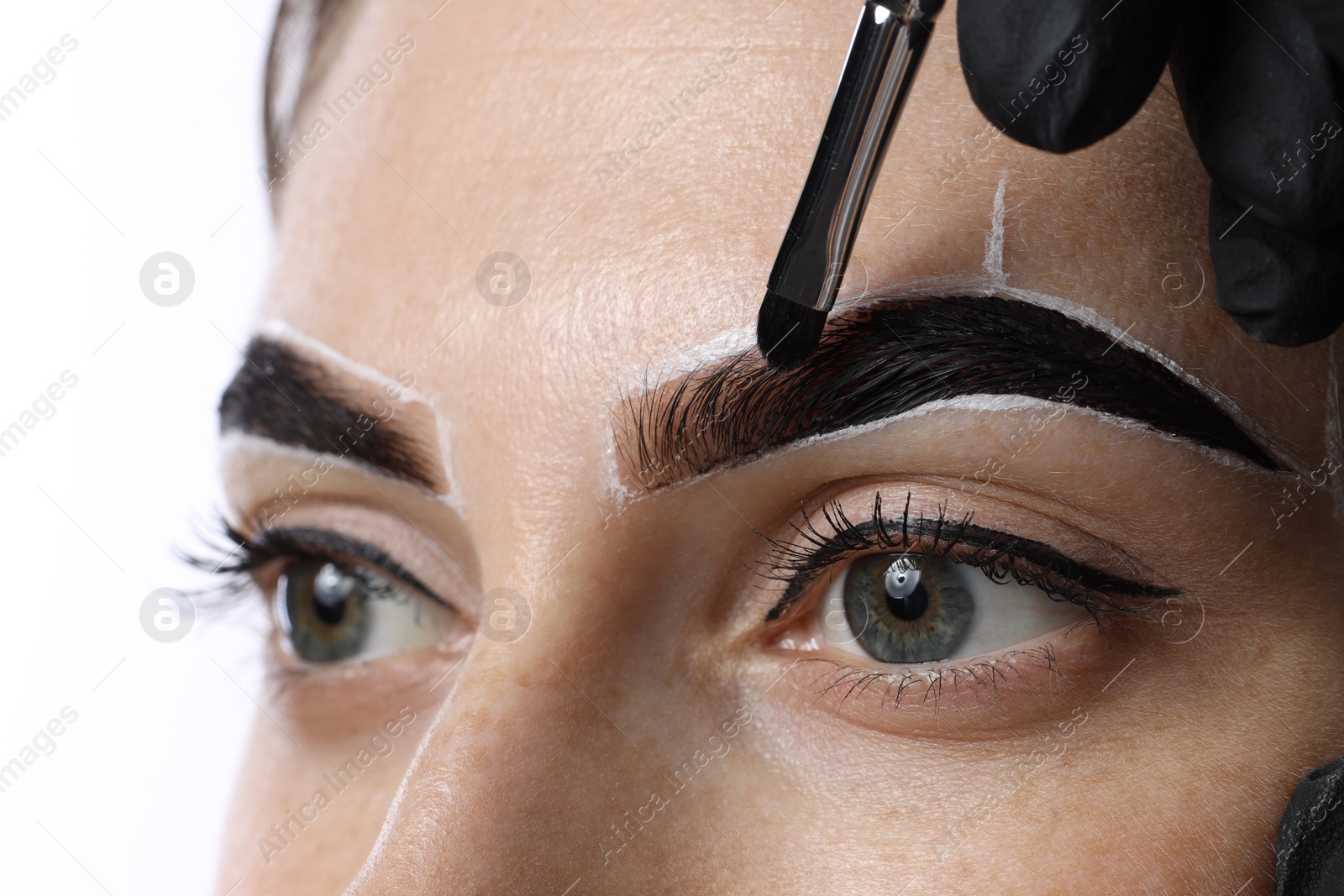 Photo of Young woman undergoing henna eyebrows dyeing on light background, closeup