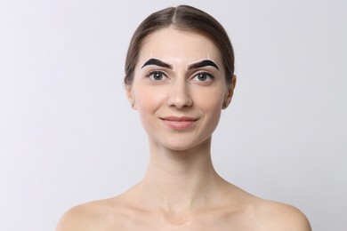 Photo of Beautiful young woman during henna eyebrows dyeing procedure on light background