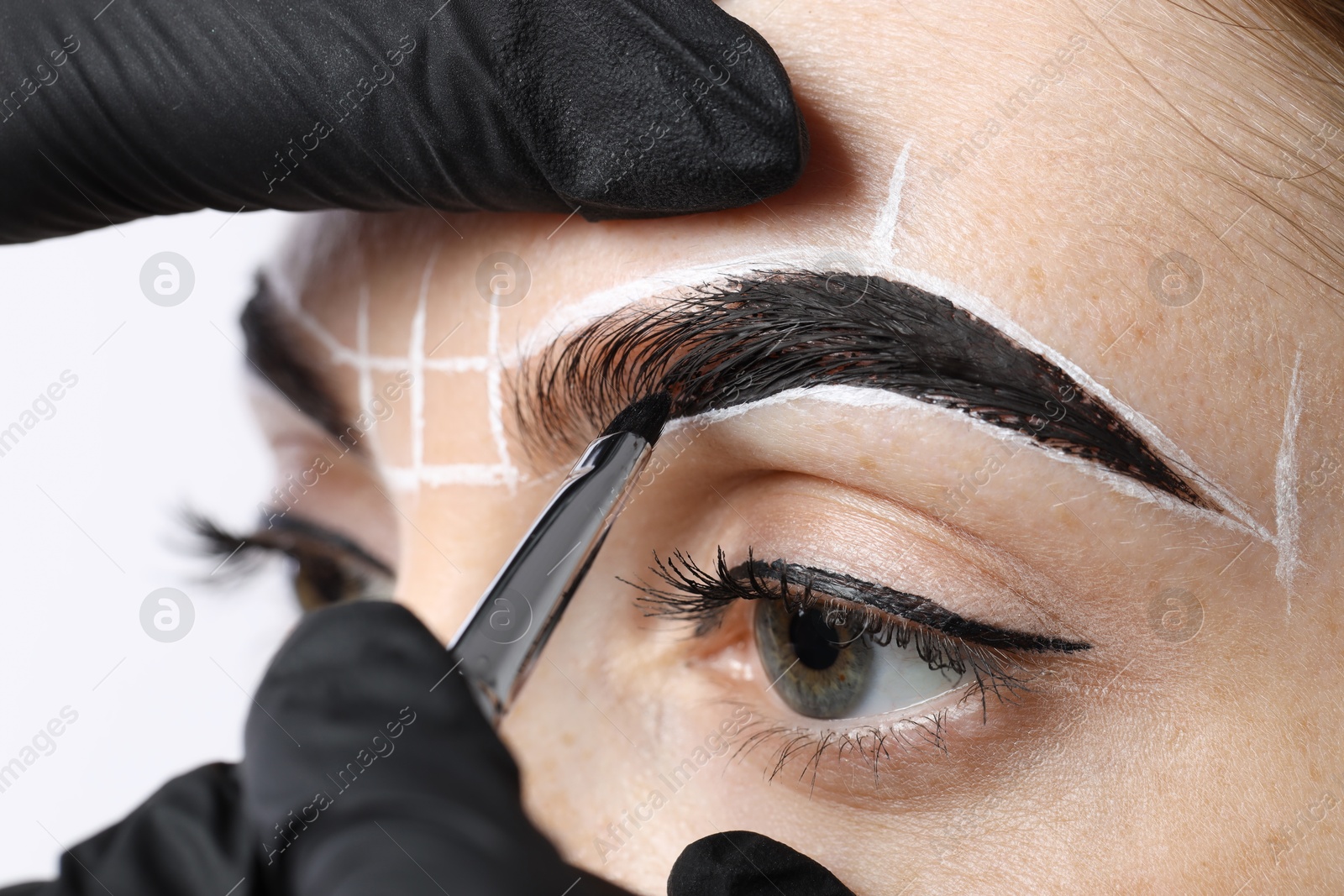 Photo of Young woman undergoing henna eyebrows dyeing procedure on light background, closeup