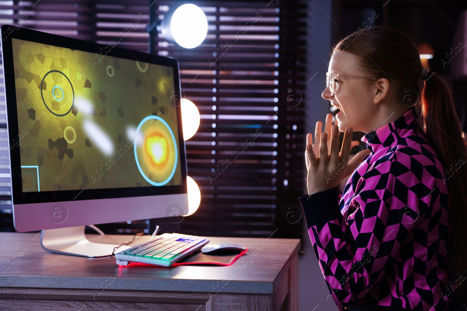 Photo of Happy girl playing video game with keyboard and mouse at table indoors