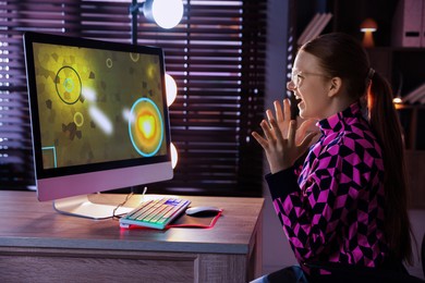 Photo of Happy girl playing video game with keyboard and mouse at table indoors