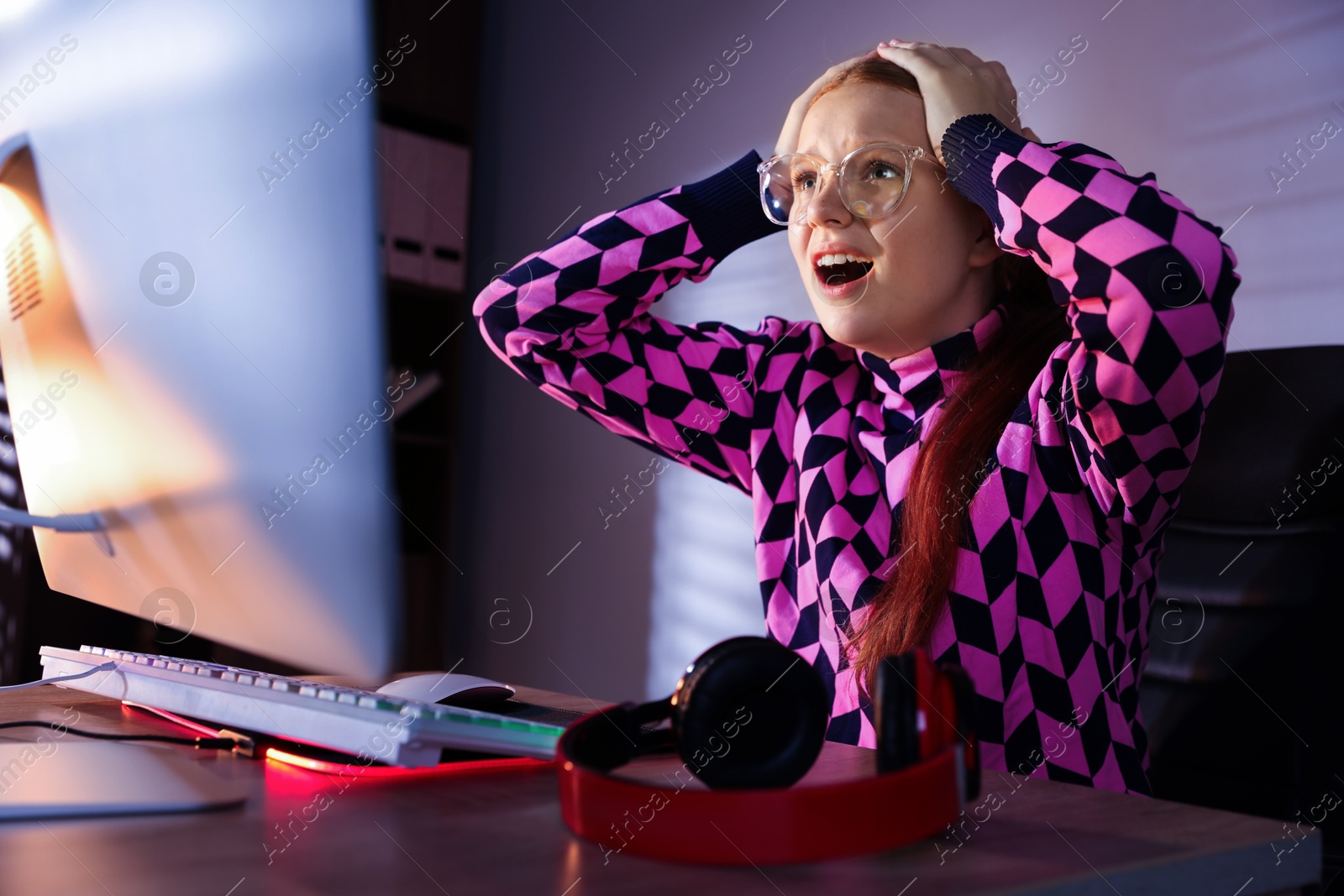 Photo of Emotional girl playing video game with keyboard at table indoors