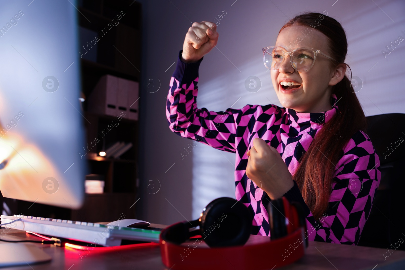 Photo of Happy girl playing video game with keyboard at table indoors